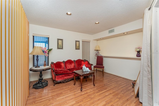 living area featuring visible vents, a textured ceiling, baseboards, and wood finished floors