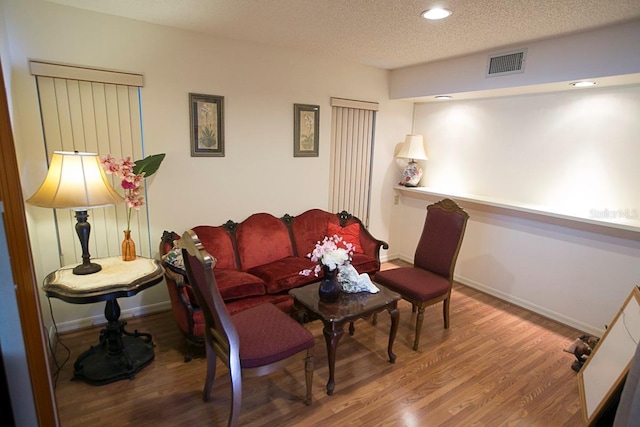 living area with baseboards, a textured ceiling, visible vents, and wood finished floors