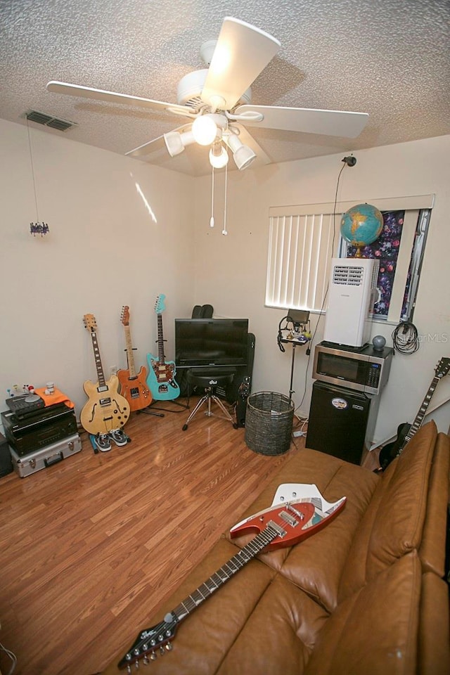 living room featuring a ceiling fan, a textured ceiling, visible vents, and wood finished floors