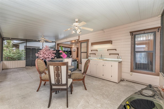 dining room with a healthy amount of sunlight, wooden walls, and a ceiling fan