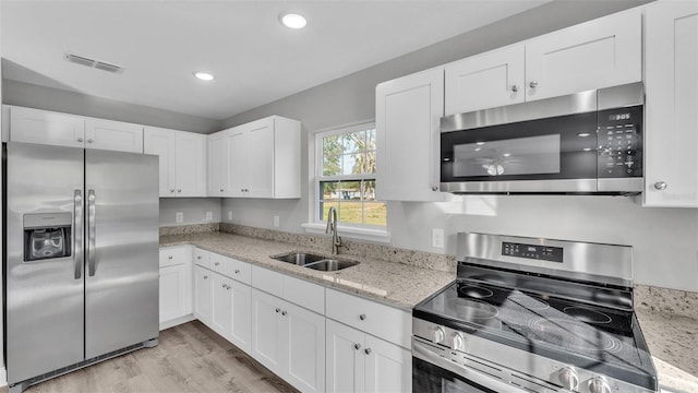 kitchen with white cabinetry, stainless steel appliances, sink, and light stone counters