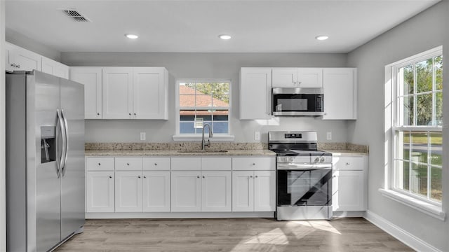 kitchen with stainless steel appliances, white cabinetry, light stone countertops, and sink