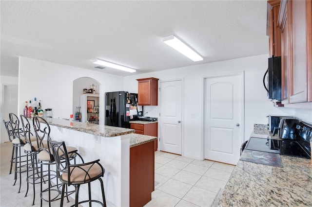 kitchen featuring a kitchen bar, kitchen peninsula, light stone counters, a textured ceiling, and black appliances