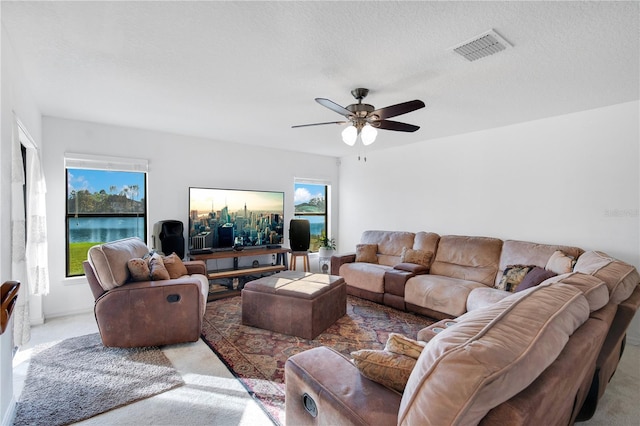 carpeted living room with a textured ceiling, a water view, plenty of natural light, and ceiling fan