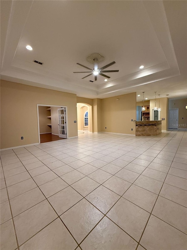 empty room featuring ceiling fan, light tile patterned flooring, and a raised ceiling