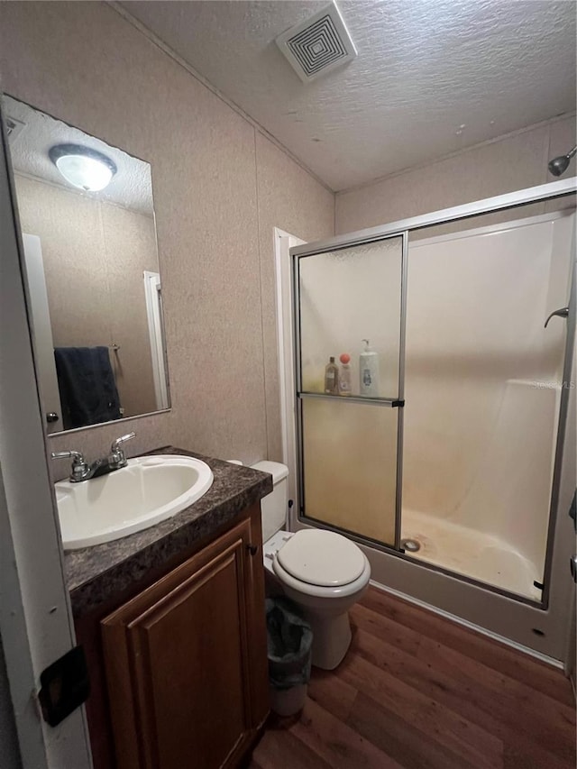 bathroom with hardwood / wood-style floors, a textured ceiling, an enclosed shower, toilet, and vanity