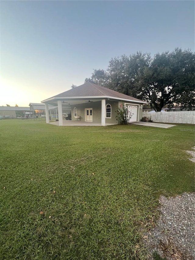 back house at dusk featuring a lawn, ceiling fan, and a garage