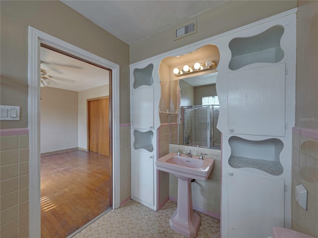 bathroom with hardwood / wood-style floors, ceiling fan, tiled shower, and tile walls