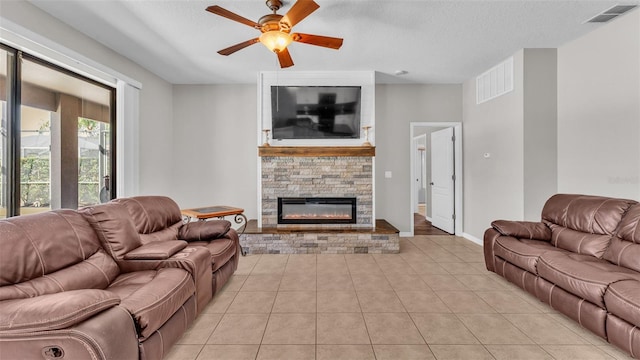 tiled living room with a textured ceiling, ceiling fan, and a fireplace