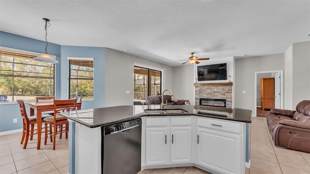 kitchen with stainless steel dishwasher, sink, decorative light fixtures, white cabinets, and a stone fireplace