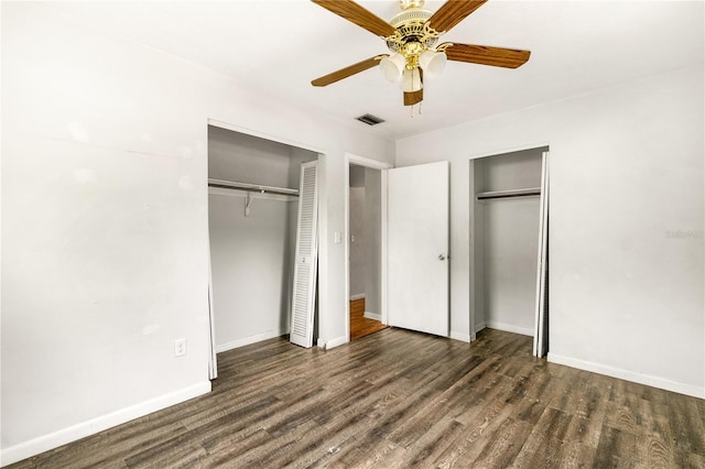 unfurnished bedroom with two closets, ceiling fan, and dark wood-type flooring