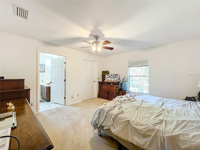 bedroom with a textured ceiling, ensuite bathroom, ceiling fan, and light carpet