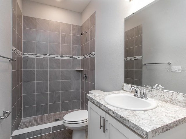 bathroom featuring a tile shower, vanity, and toilet