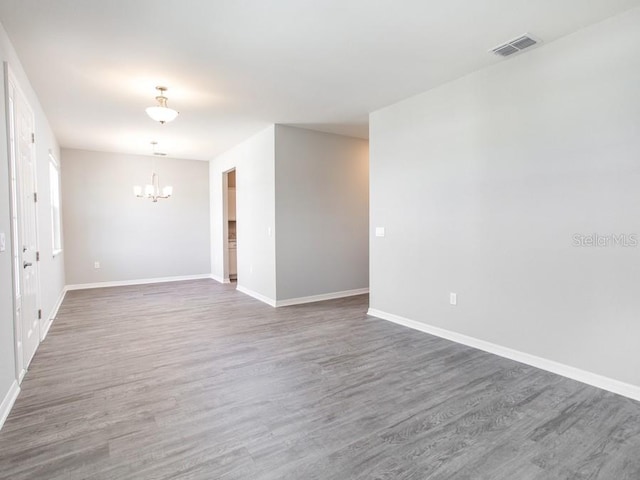 spare room with a chandelier and dark wood-type flooring