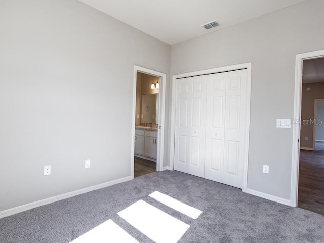 unfurnished bedroom featuring dark colored carpet, a closet, and ensuite bath