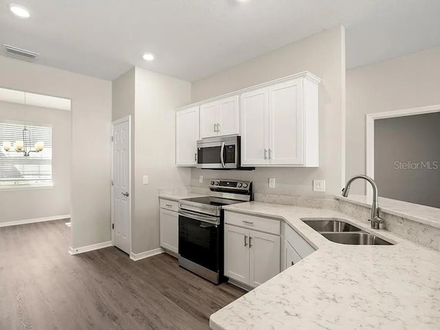 kitchen featuring dark wood-style floors, stainless steel appliances, a sink, light stone countertops, and white cabinetry