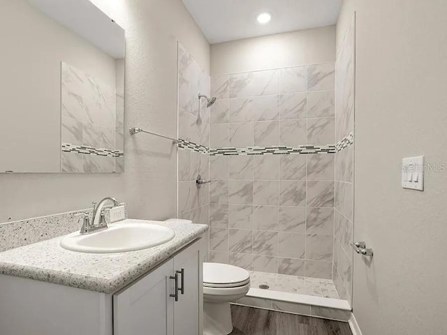 bathroom featuring wood finished floors, vanity, toilet, and tiled shower