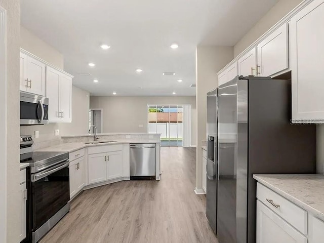 kitchen with white cabinets, light wood finished floors, a sink, a peninsula, and appliances with stainless steel finishes
