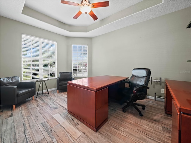 home office featuring a raised ceiling, ceiling fan, and light wood-type flooring