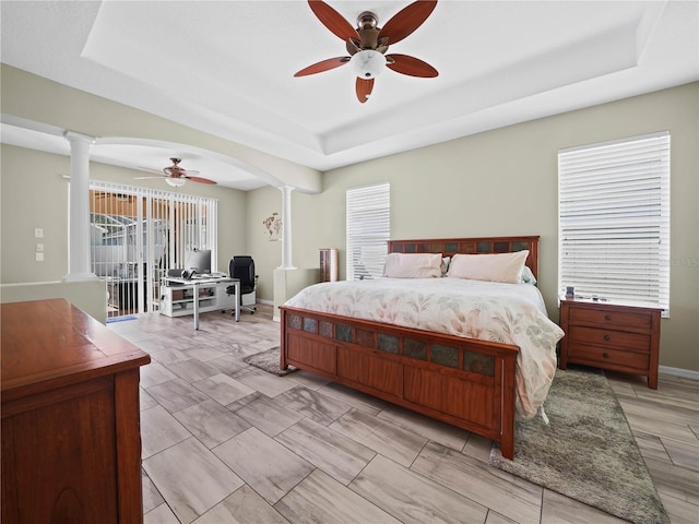 bedroom featuring a raised ceiling, ornate columns, ceiling fan, and access to outside