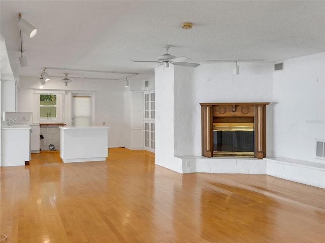 unfurnished living room with a textured ceiling, track lighting, and light hardwood / wood-style floors