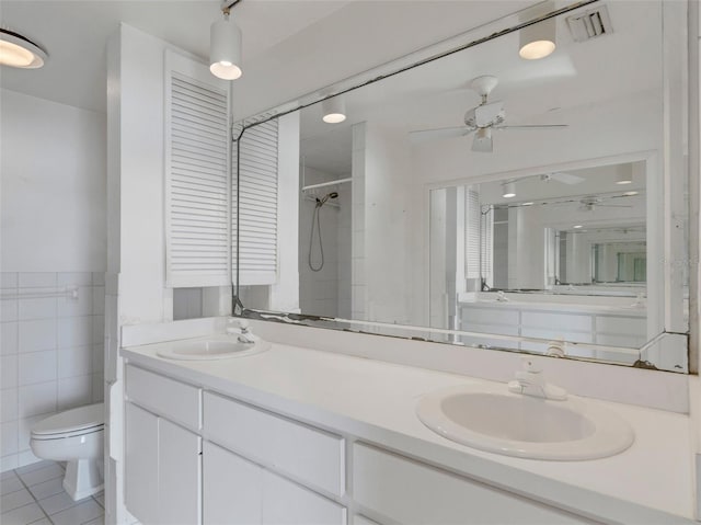 bathroom with vanity, tile patterned floors, toilet, tiled shower, and tile walls