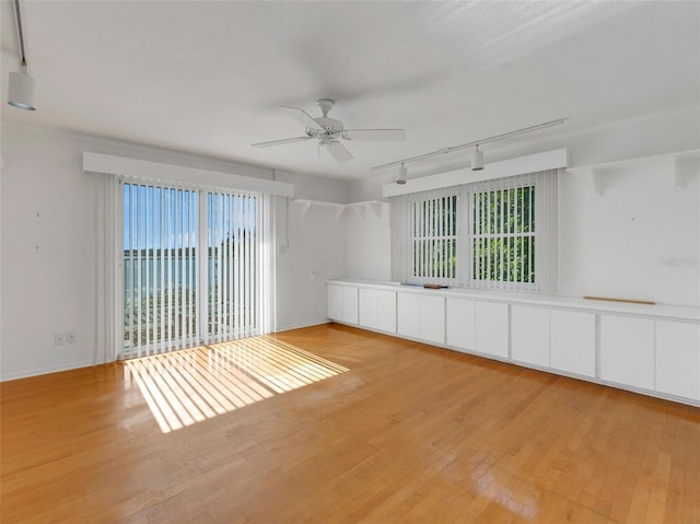 spare room with plenty of natural light, light hardwood / wood-style floors, rail lighting, and ceiling fan