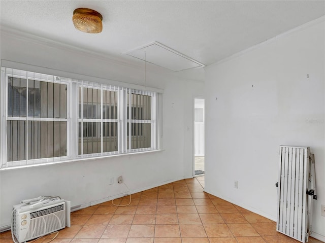 empty room with a wall mounted air conditioner, light tile patterned floors, a textured ceiling, ornamental molding, and radiator heating unit