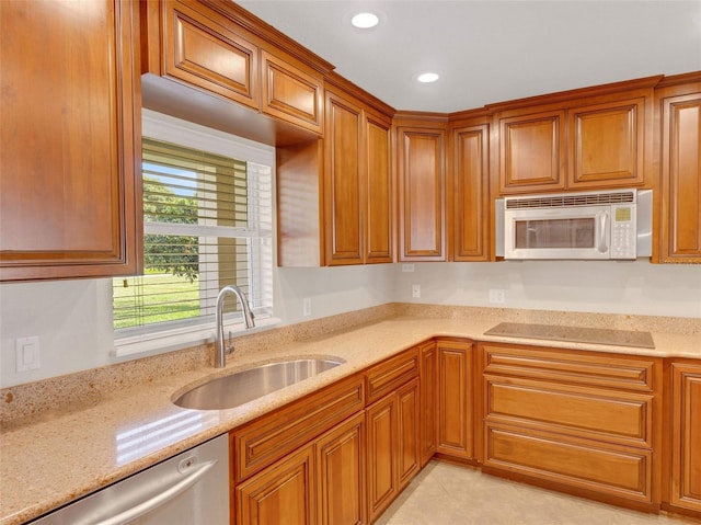 kitchen with light stone countertops, black electric cooktop, sink, light tile patterned floors, and dishwasher