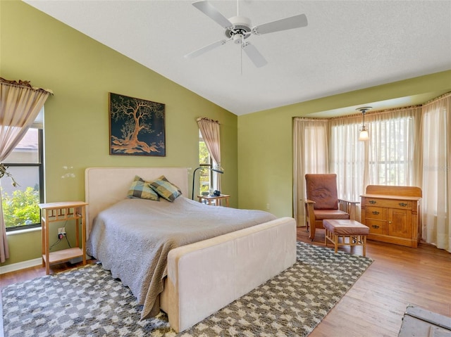 bedroom featuring ceiling fan, vaulted ceiling, a textured ceiling, and light hardwood / wood-style flooring