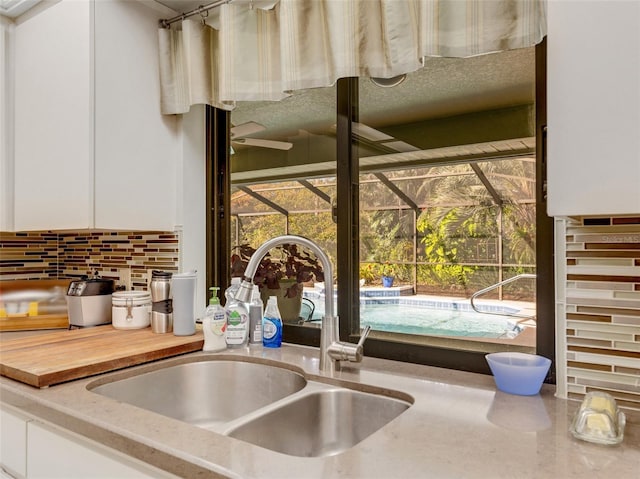 interior details with tasteful backsplash, white cabinetry, and sink