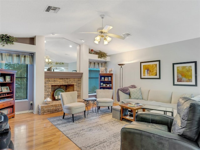 living room with a brick fireplace, a healthy amount of sunlight, light wood-type flooring, and vaulted ceiling