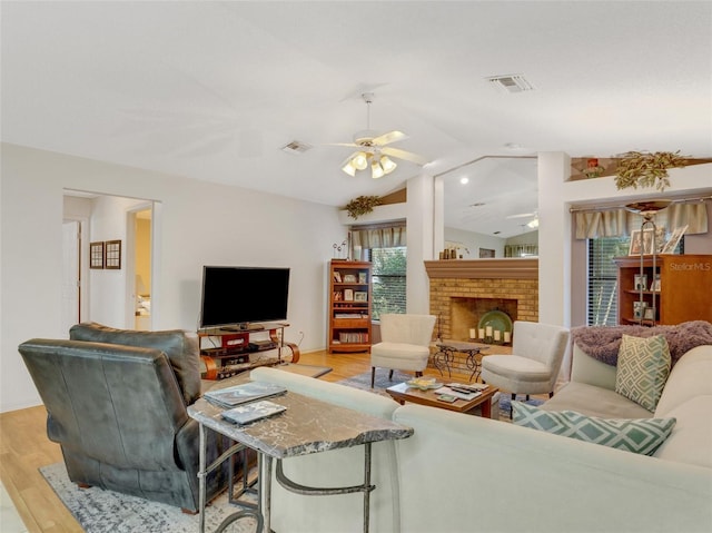 living room with ceiling fan, light hardwood / wood-style floors, a fireplace, and vaulted ceiling