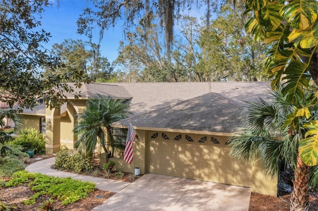 view of front of property with concrete driveway, a shingled roof, an attached garage, and stucco siding