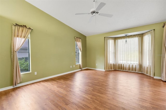 empty room featuring lofted ceiling, wood finished floors, a ceiling fan, and baseboards