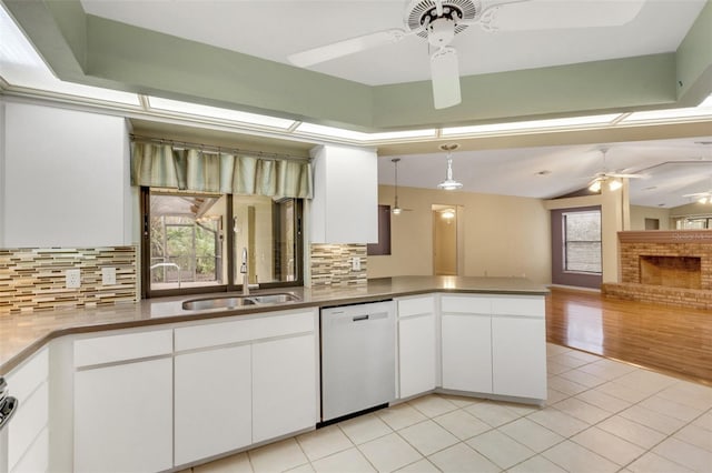 kitchen with light tile patterned floors, white dishwasher, a peninsula, a sink, and a ceiling fan