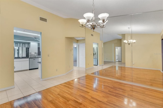 spare room featuring light wood-style flooring, ceiling fan with notable chandelier, visible vents, baseboards, and vaulted ceiling