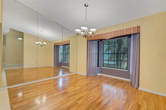 spare room with a chandelier, wood finished floors, and baseboards