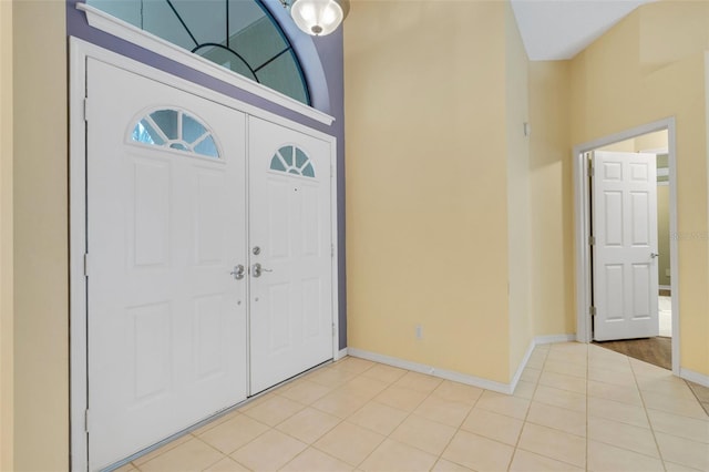 foyer entrance with a towering ceiling, light tile patterned floors, and baseboards