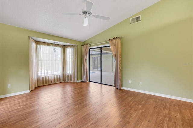 empty room with vaulted ceiling, wood finished floors, visible vents, and baseboards