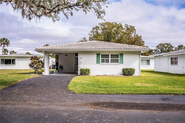 ranch-style home featuring an attached carport, stucco siding, a front lawn, aphalt driveway, and a tiled roof