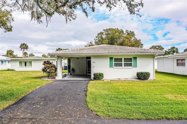 ranch-style home featuring aphalt driveway, an attached carport, a front yard, and a tiled roof