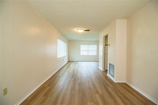 spare room featuring baseboards, wood finished floors, visible vents, and a textured ceiling