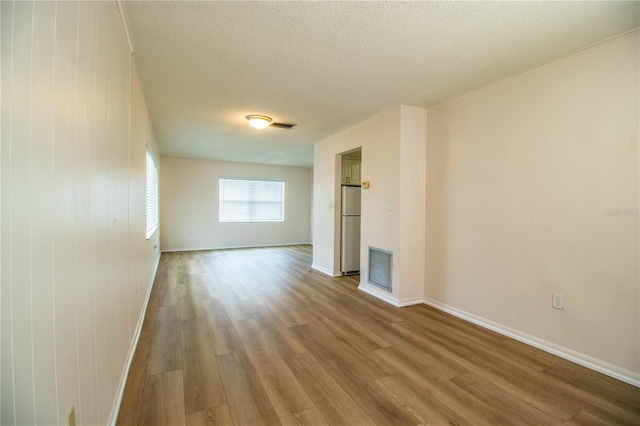 empty room featuring baseboards, wood finished floors, visible vents, and a textured ceiling