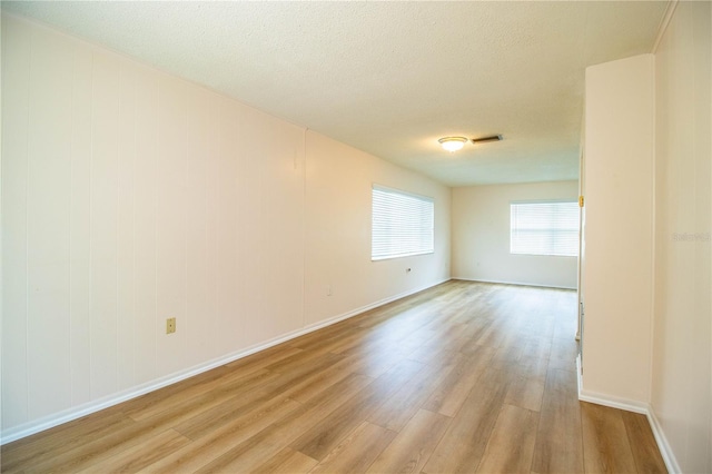 empty room with light wood-style flooring, baseboards, and a textured ceiling