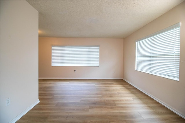 empty room featuring light wood-style floors, baseboards, and a textured ceiling