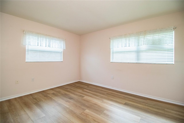 unfurnished room with light wood finished floors, a healthy amount of sunlight, and baseboards