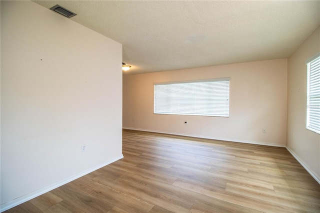 spare room with visible vents, a textured ceiling, light wood-type flooring, and baseboards