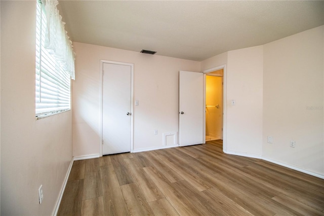 unfurnished bedroom with wood finished floors, visible vents, and baseboards