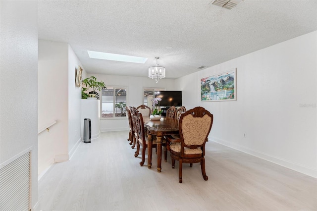 dining room with a textured ceiling, a skylight, wood finished floors, and visible vents